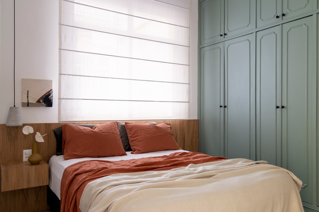 Quarto com armários azuis, cama de casal com cabeceira de madeira e cortina.