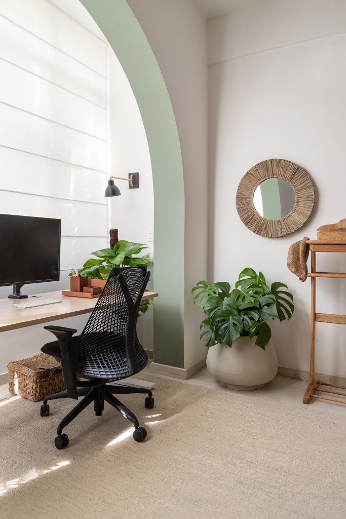 Home office com mesa de madeira sob arco de alvenaria e plantas