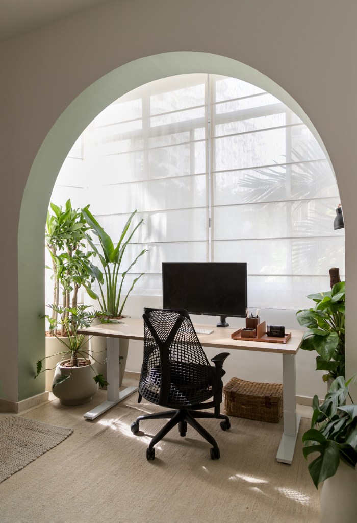 Home office com mesa de madeira sob arco de alvenaria e plantas