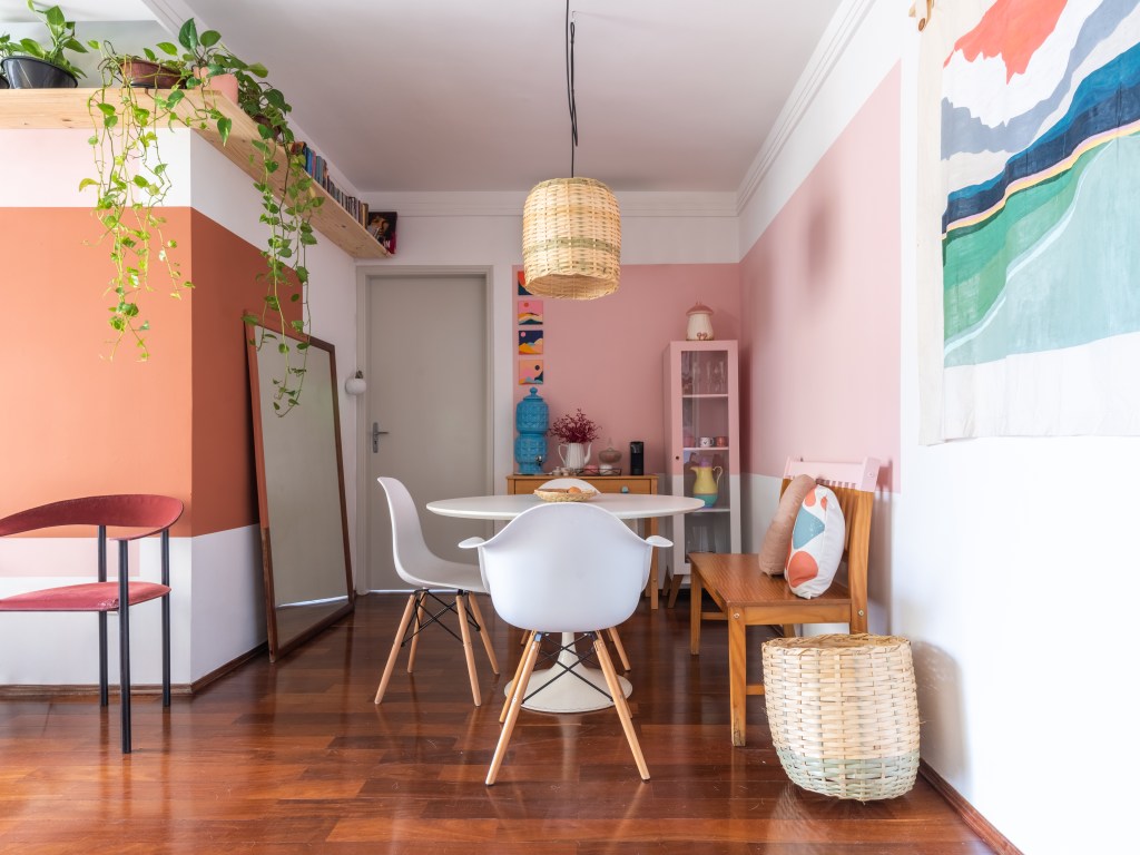 Sala de jantar com parede rosa, mesa redonda branca e luminária de palha.
