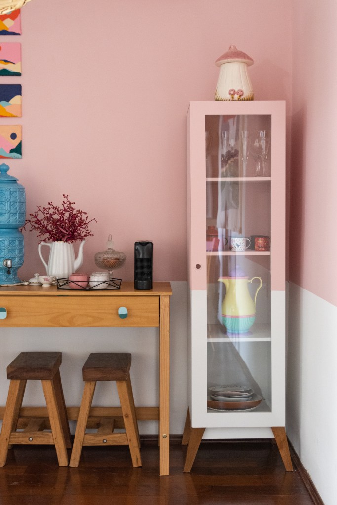 Sala de estar com meia parede rosa, aparador de madeira e cristaleira.