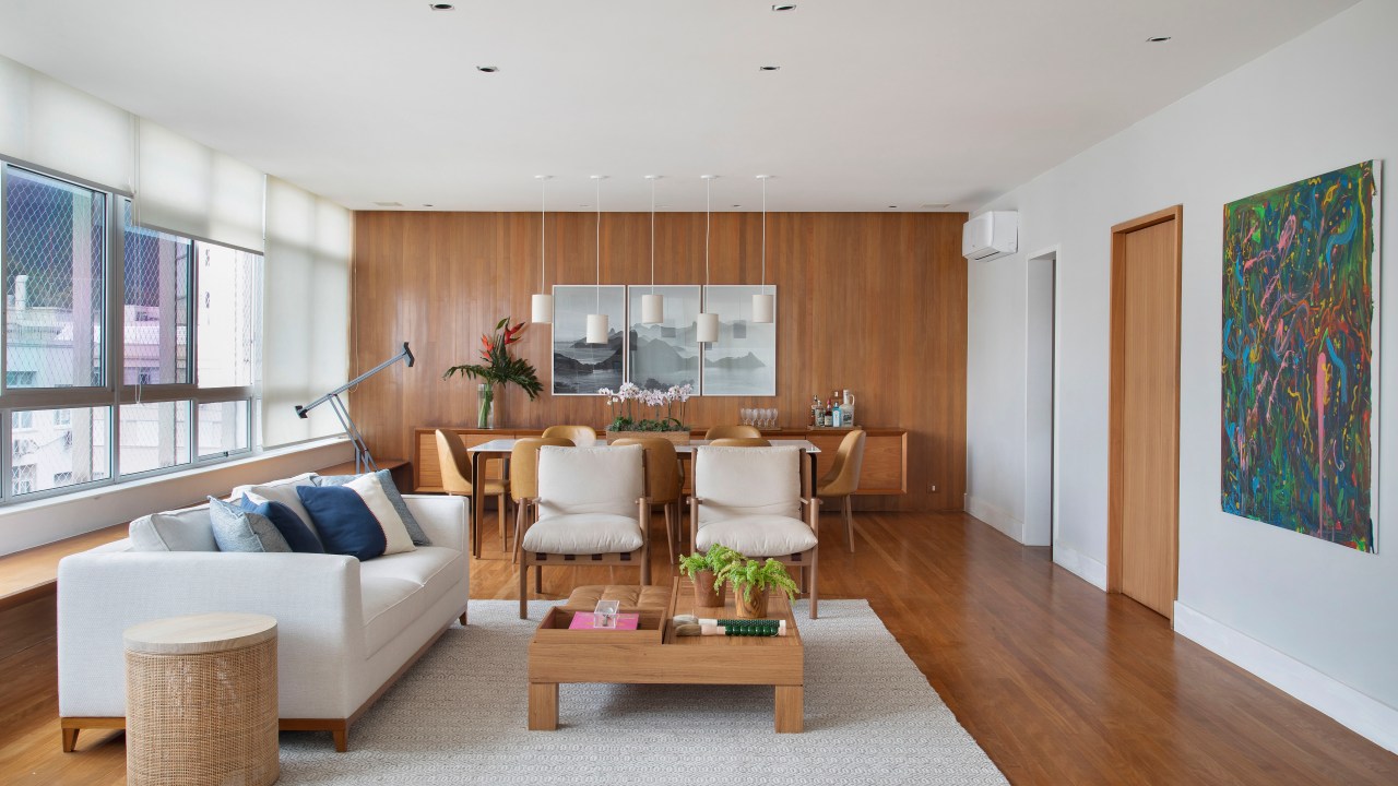 Sala de estar integrada com jantar com sofá branco, mesa de centro de madeira, mesa de jantar e cadeiras terracota.