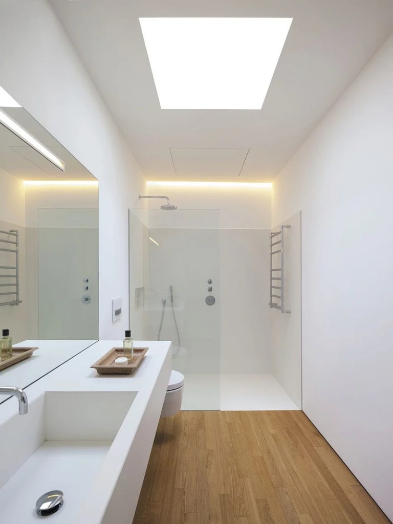 Banheiro minimalista com revestimentos brancos e box de vidro.