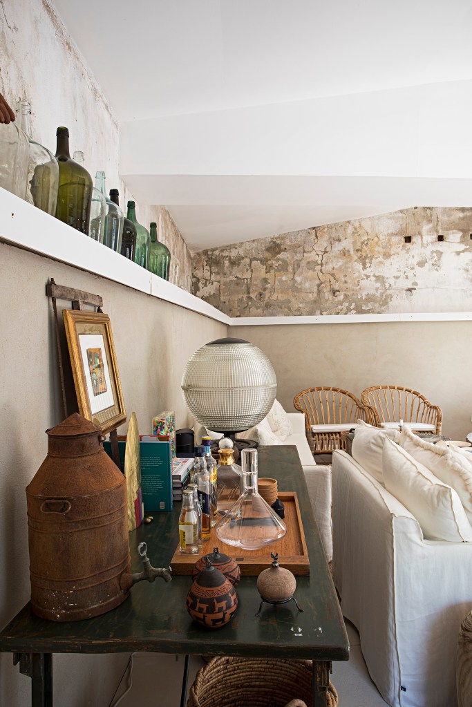 Sala de estar rústica com sofás brancos, mesa de centro baú, parede exposta e prateleira com garrafas