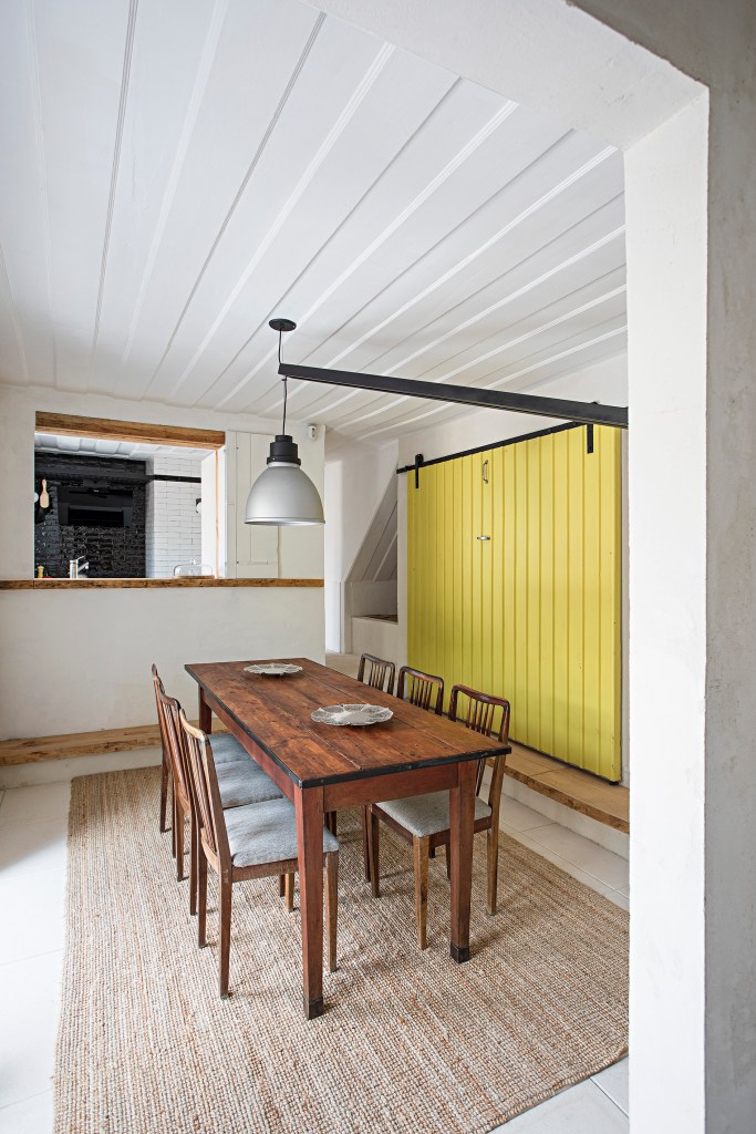 Sala de jantar com porta amarela, mesa de madeira e luminária grande de piso.