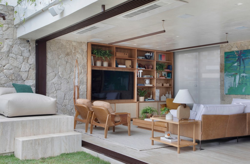 Cobertura integrada com jardim; sala de estar com poltronas, sofá, estante para tv e parede de pedra.