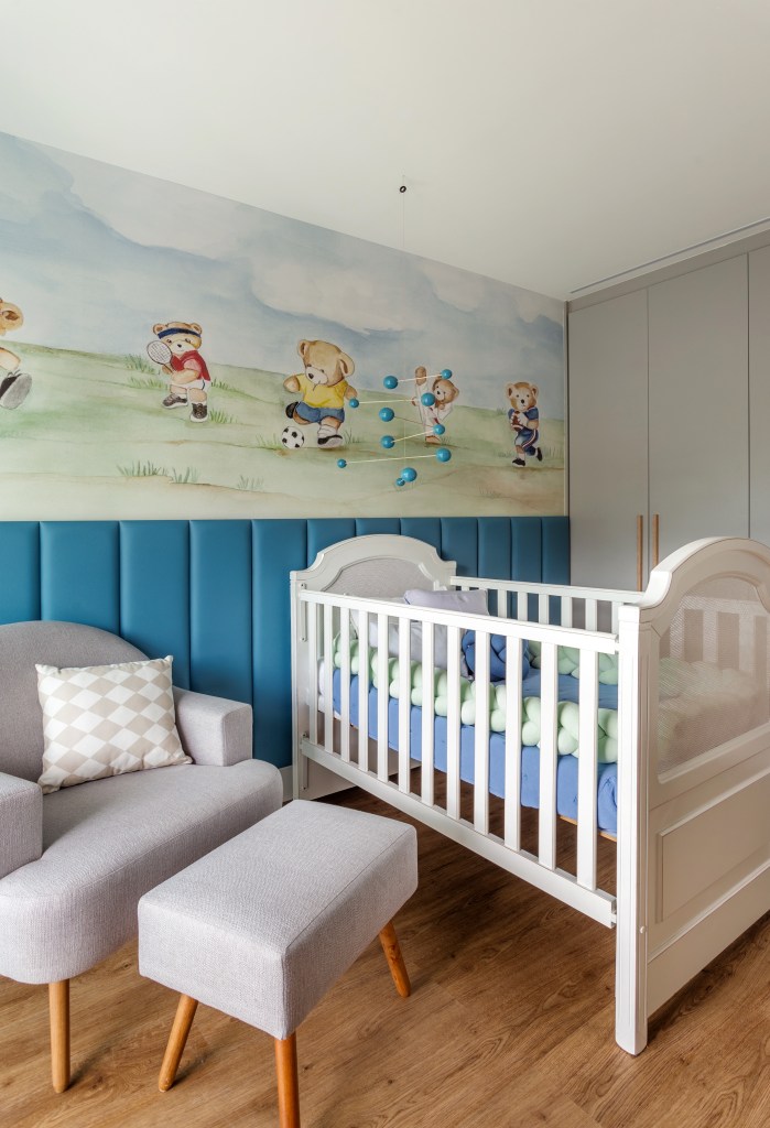 Quarto de bebê com papel de parede, marcenaria clara, berço e meia parede azul.