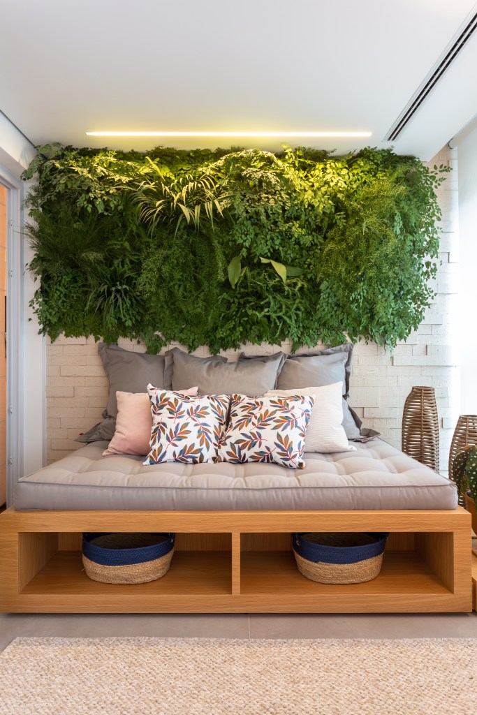 Varanda integrada com jardim vertical e futon cinza.