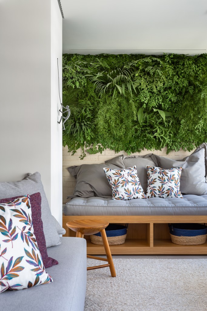 Varanda integrada com jardim vertical e futon cinza.
