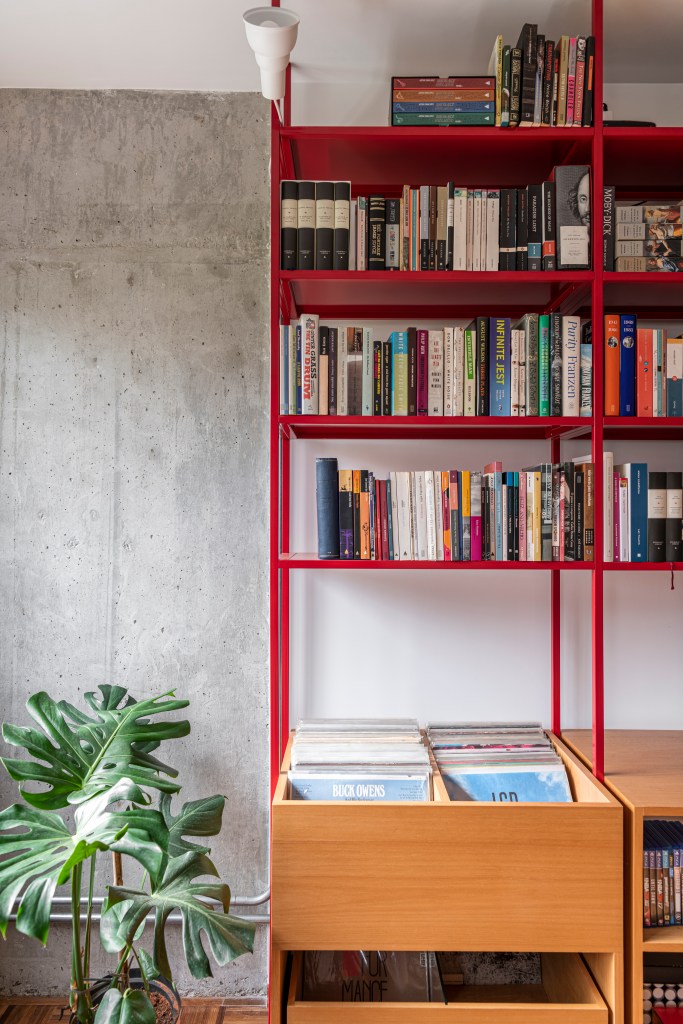 Estante de serralheria vermelha com livros, banco e espaço para discos de vinil.
