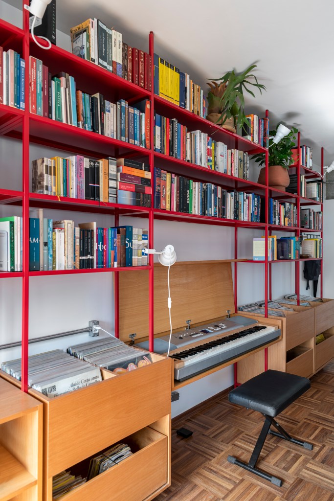 Estante de serralheria vermelha com livros, banco e espaço para discos de vinil.