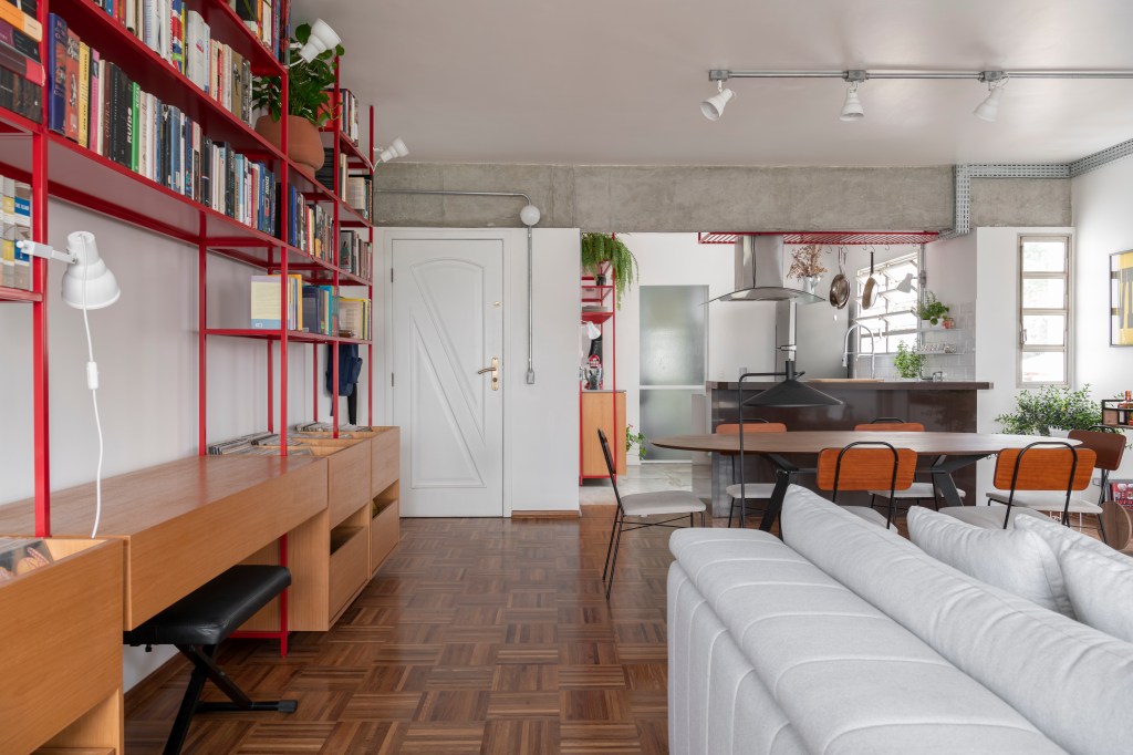 Sala de estar integrada com cozinha, estante de serralheria de madeira e iluminação com trilhos de spots.