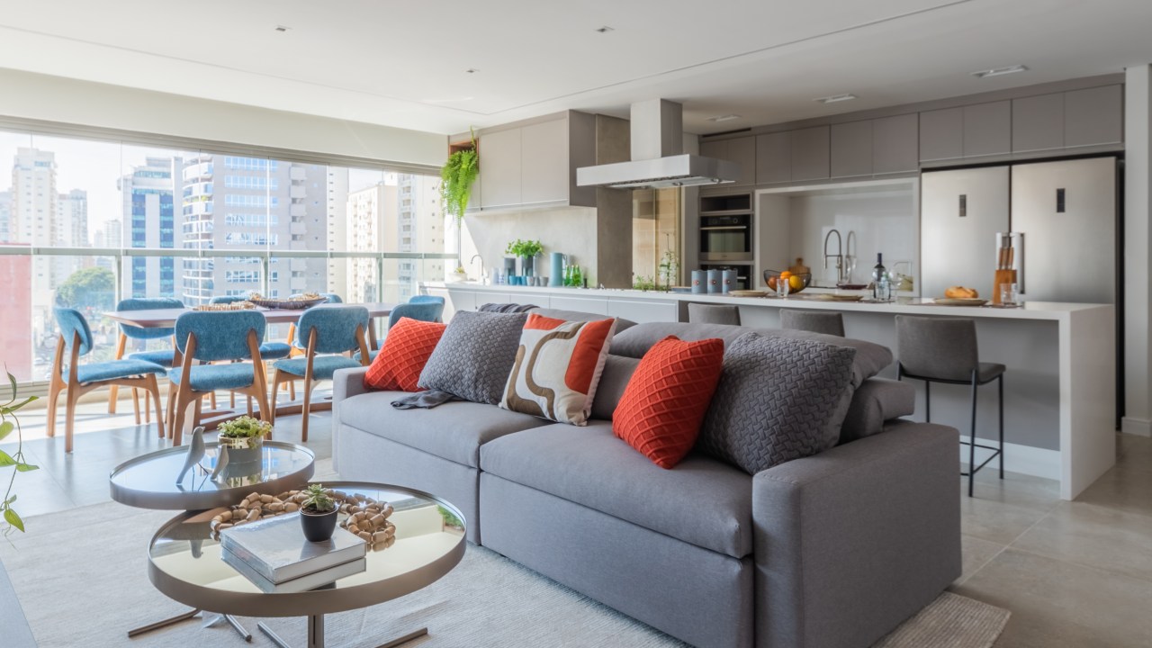 Sala de estar integrada com cozinha com sofá cinza, mesa de centro e tapete claro