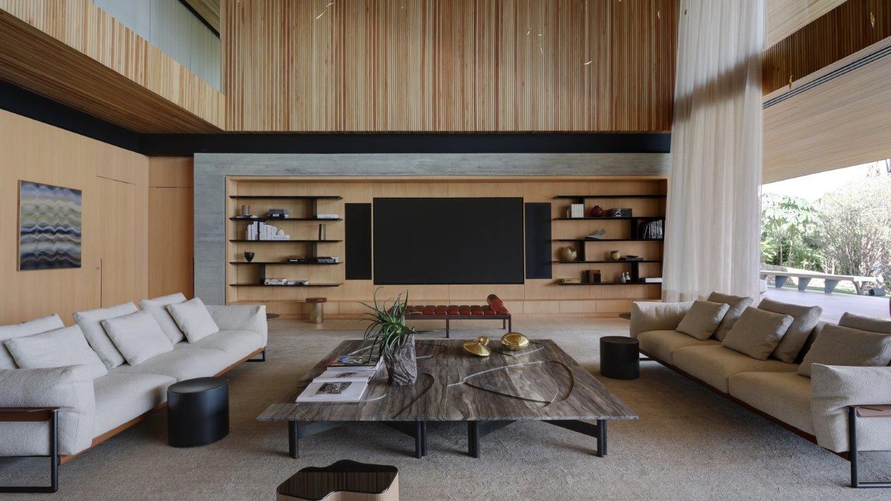 Sala de estar com pé-direito duplo, revestimentos em madeira, mobiliário claro, painel para tv.
