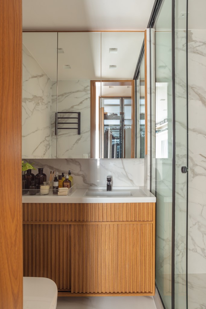 Banheiro com revestimento de mármore, box de vidro e armários de madeira.