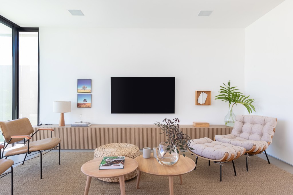 Sala de estar; sala de tv com tapete bege, poltrona, sofá branco, mesa de centro de madeira.