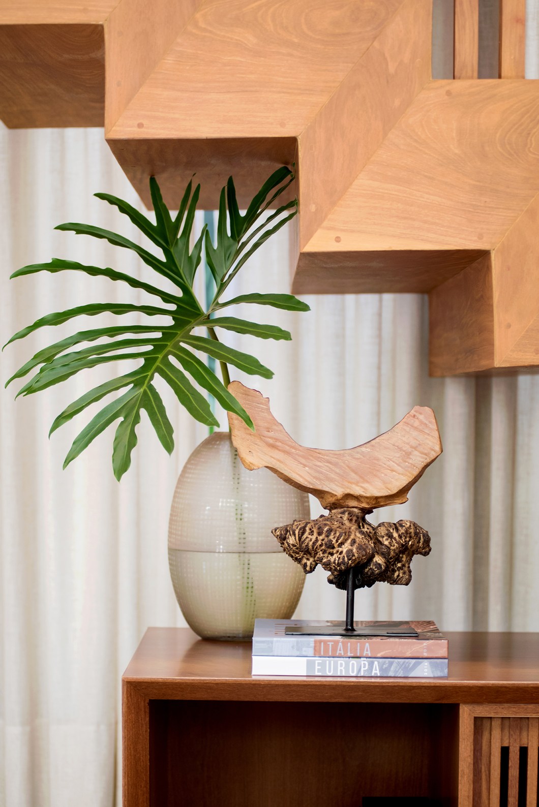 Em um conceito de interiores lindo e funcional, o escritório Paiva e Passarini trouxe para o living uma escultura do artista Arturo Silverio, que acompanha um o toque do natural também disposto no rack da TV.