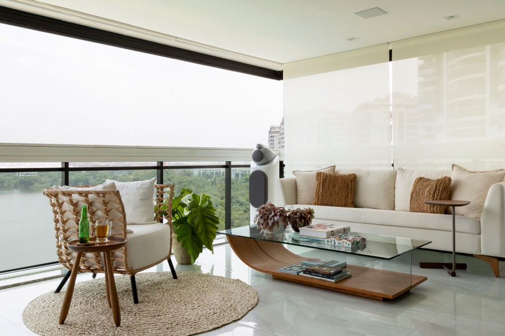 Varanda integrada com piso de porcelanato, poltrona, sofá branco e mesa de centro com tampo de vidro.