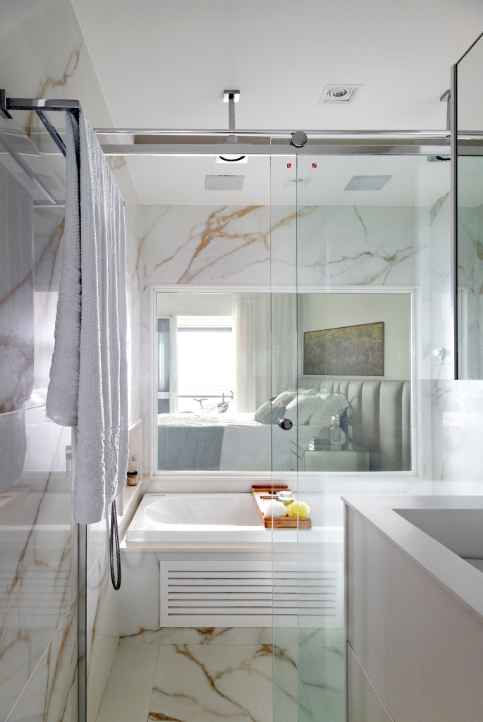 Banheiro com revestimento de mármore, box de banho e banheira.