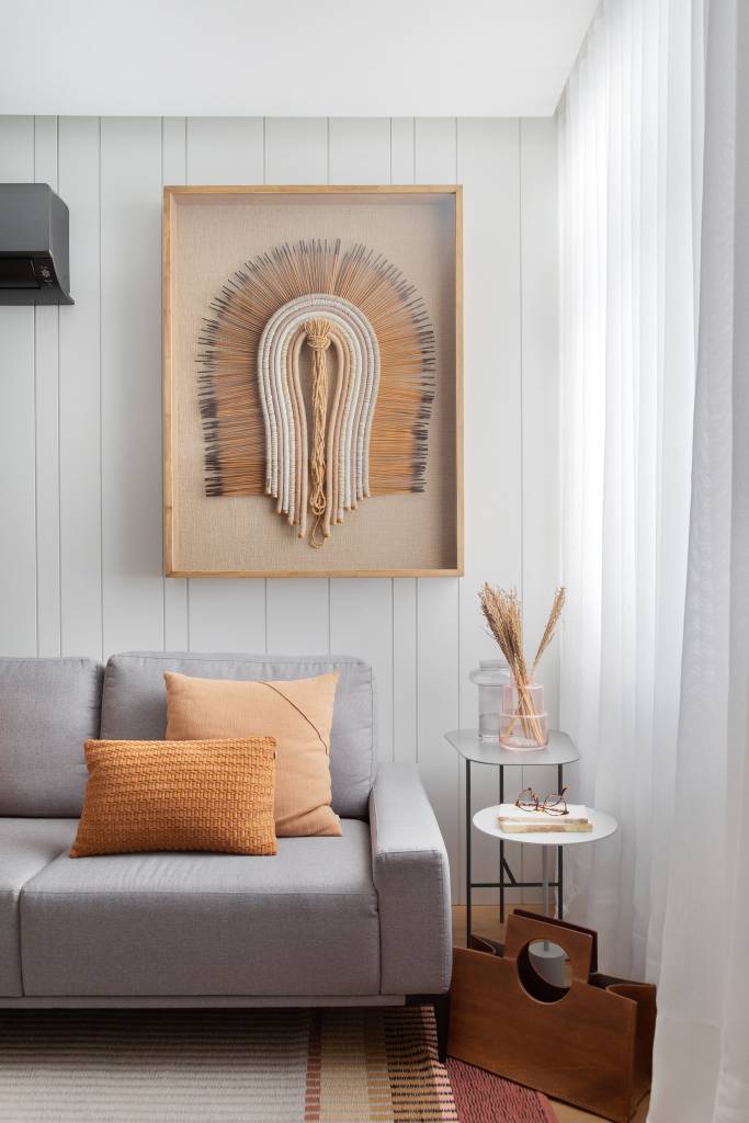 Sala de estar com sofá cinza e obra de arte com cocar em cima do sofá.