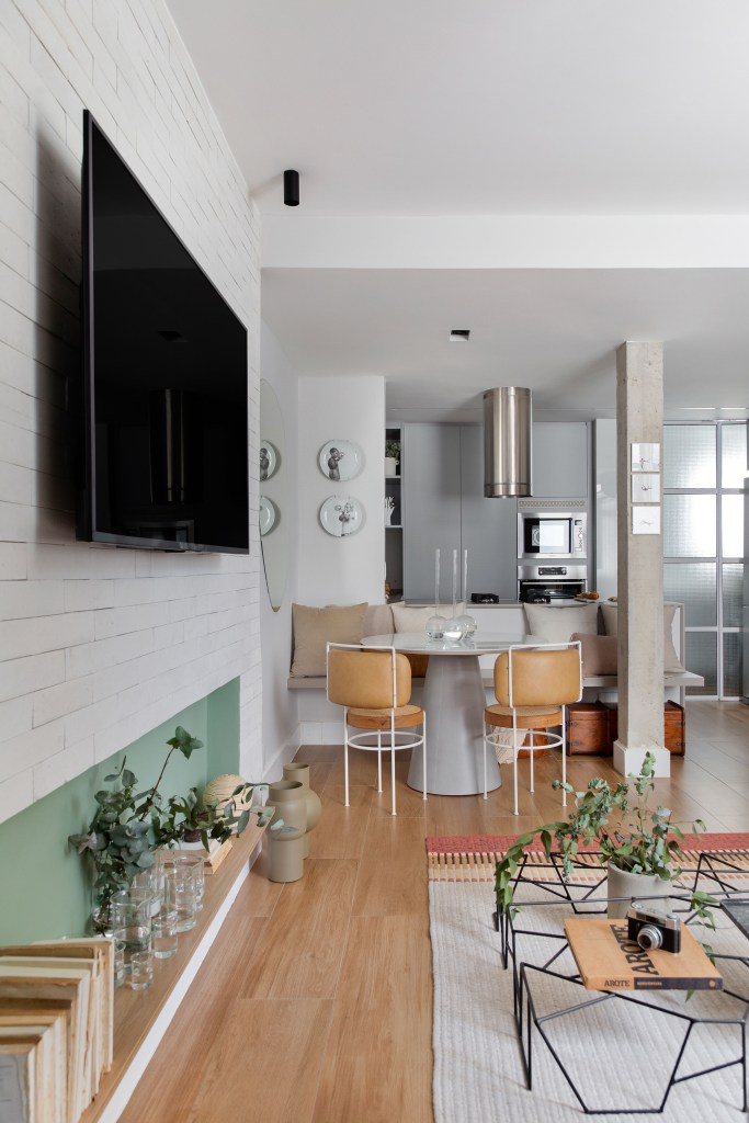 Sala de estar integrada com jantar e cozinha; piso de madeira, mesa redonda e bancada branca de cozinha.