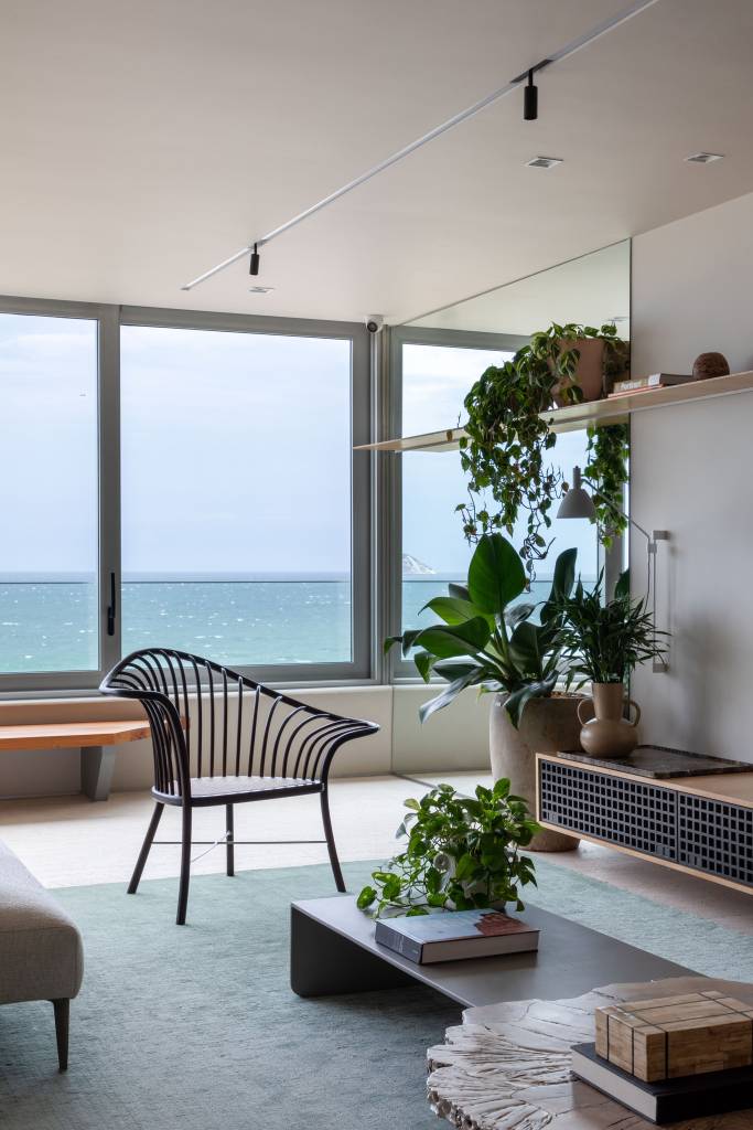 Sala de estar com janelas grandes, poltrona e prateleira com plantas.