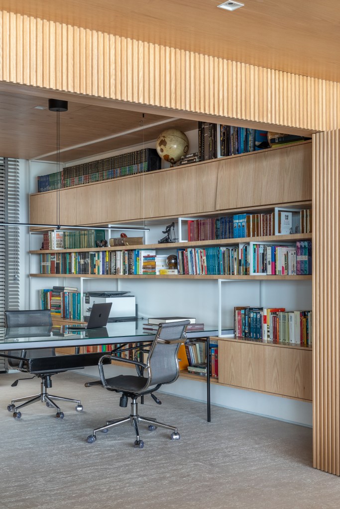 Home office; Espaço de coworking com mesa de trabalho, cadeiras de escritório, estante de madeira com livros.