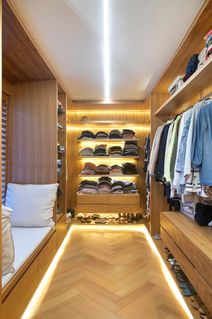 Closet com armários em madeira e prateleiras iluminadas.