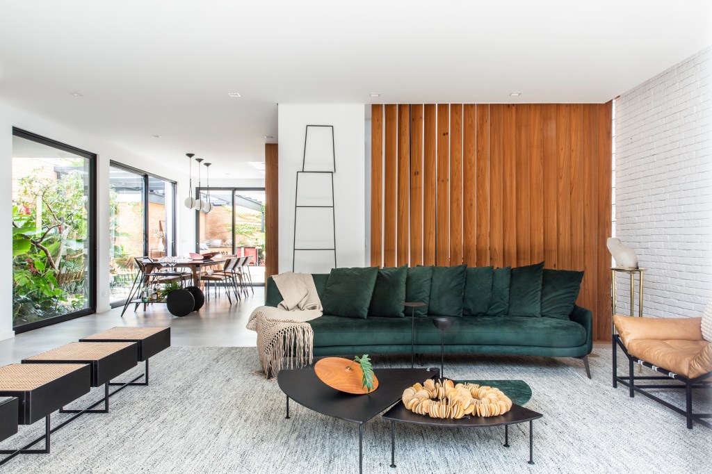 Sala de estar clara com sofá verde, mesa de centro preta, parede de madeira.