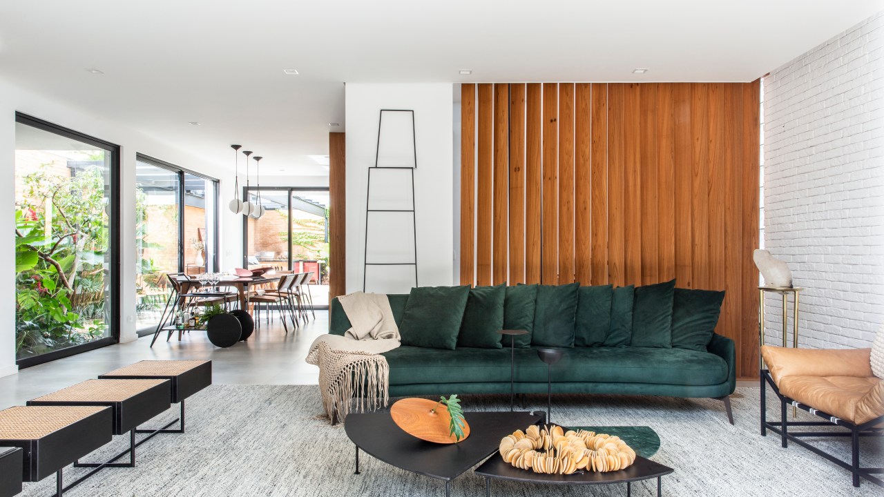 Sala de estar clara com sofá verde, mesa de centro preta, parede de madeira.