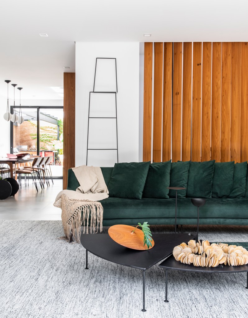 Sala de estar clara com sofá verde, poltronas, parede de tijolinhos e cortina branca.