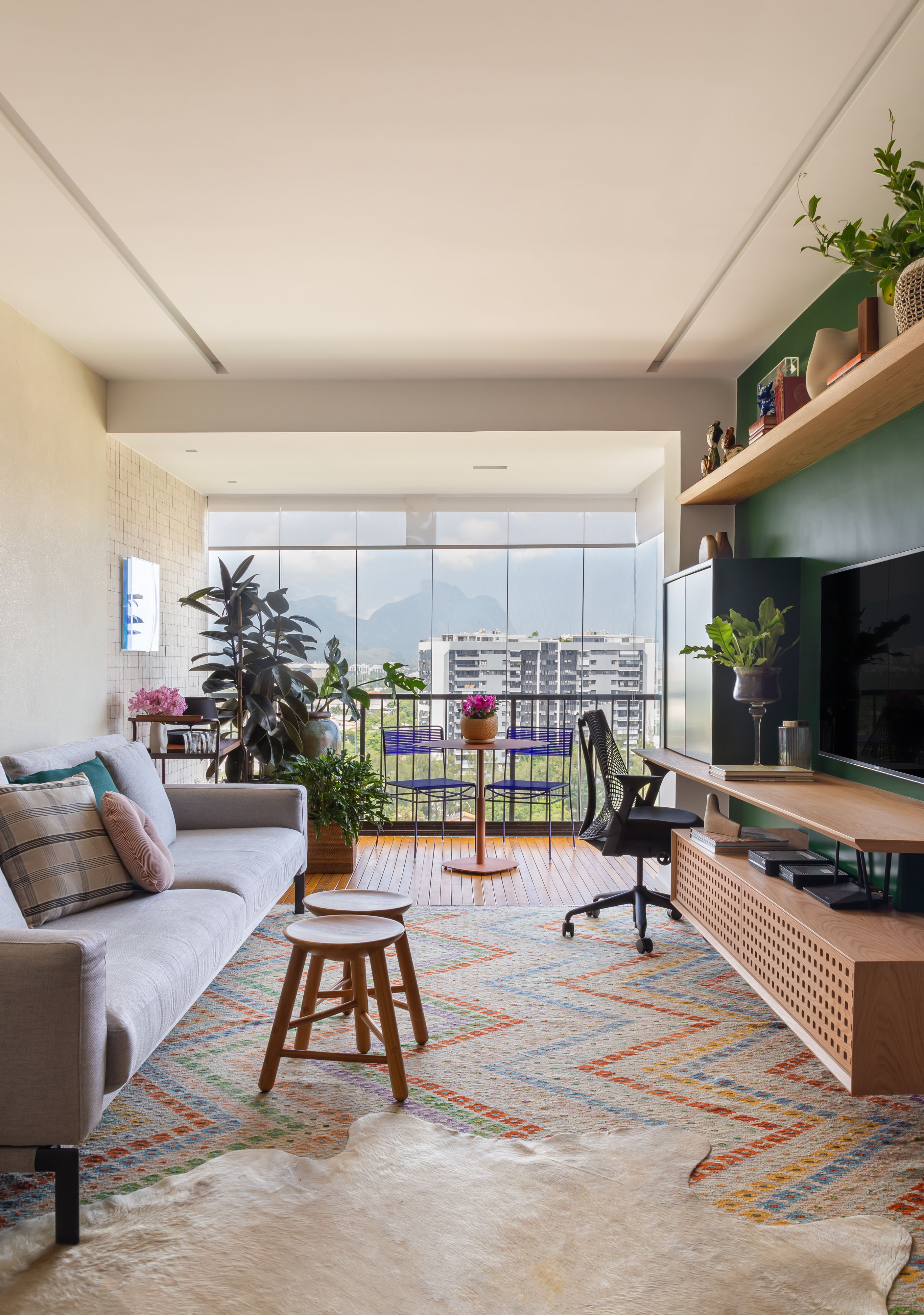 Sala de estar integrada com varanda e jantar; tapete colorido, sofá cinza e parede verde.