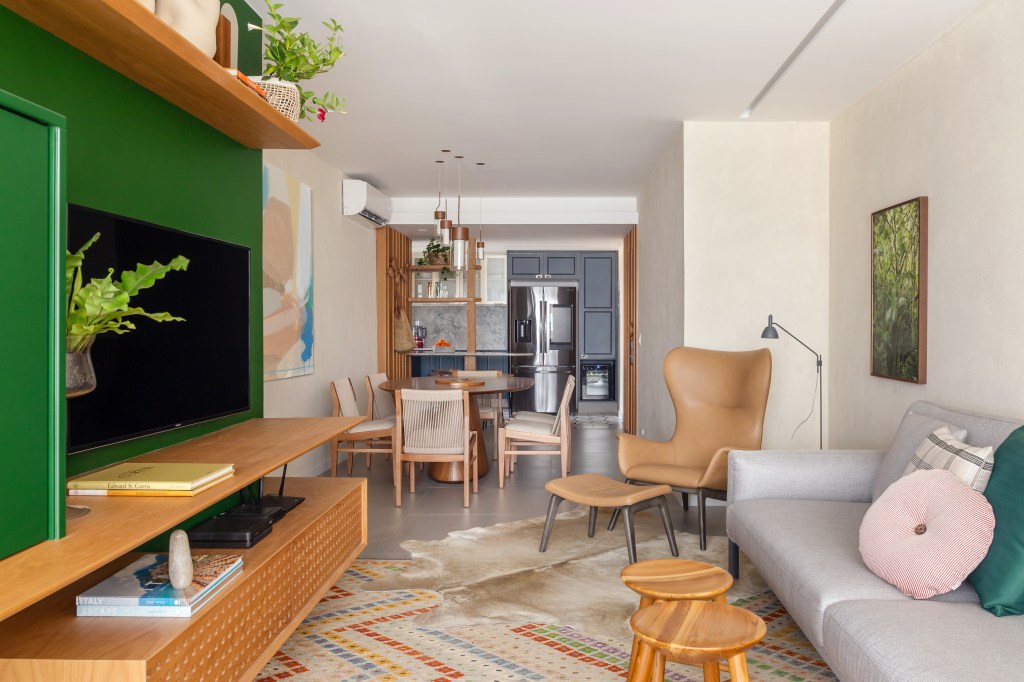 Sala de estar integrada com varanda e jantar; tapete colorido, sofá cinza e parede verde.