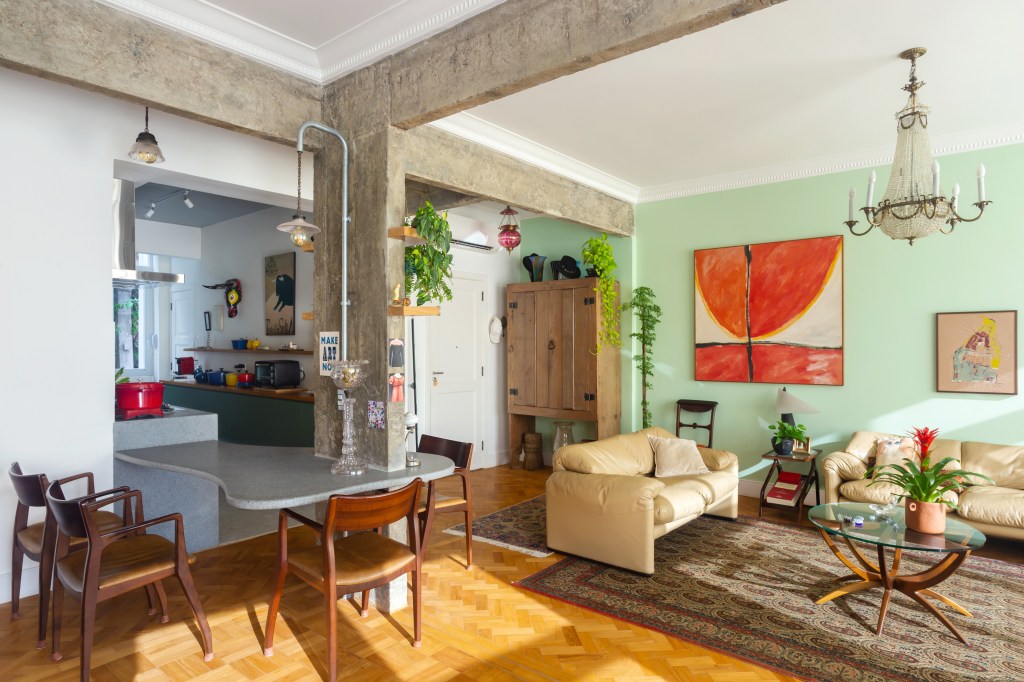 Sala de estar com decoração vintage; sofás claros, tapete estampado, lustre e parede verde.
