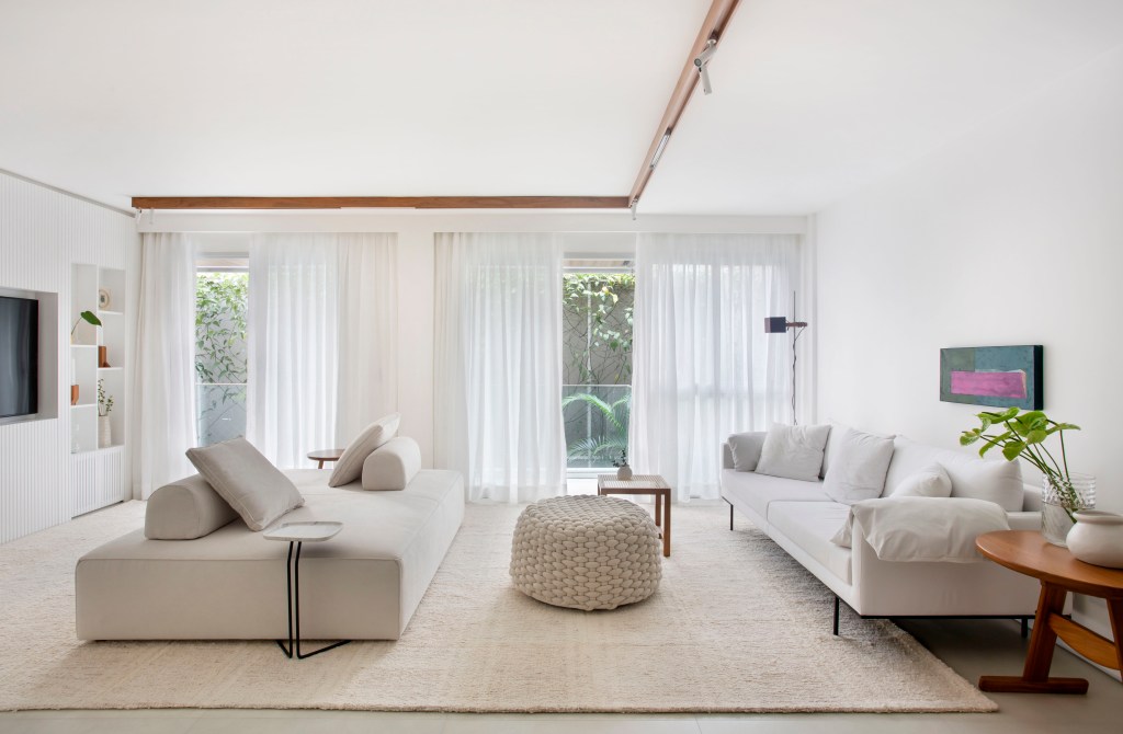 Sala de estar branca com sofá branco, sofá ilha branco, tapete off white e pufe de macramê.