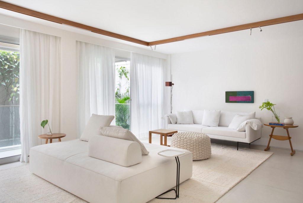 Sala de estar branca com sofá branco, sofá ilha branco, tapete off white e pufe de macramê.