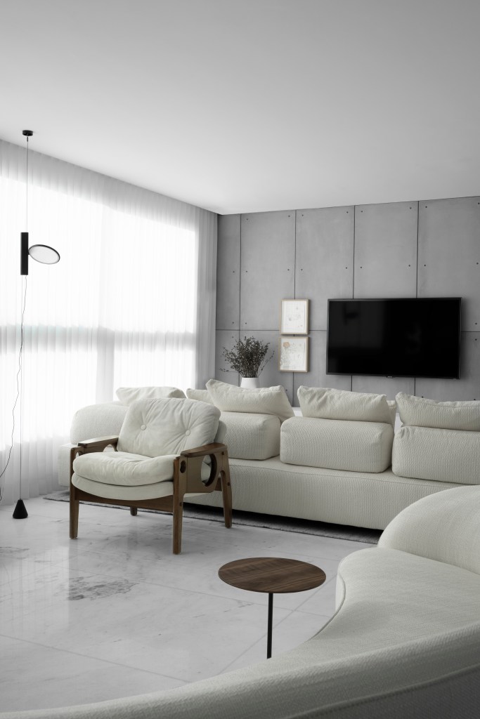 Sala de estar integrada com piso branco, sofá branco, poltrona branca e parede revestida com placas cimentícias.