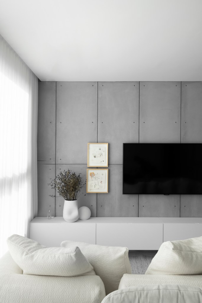 Sala de estar integrada com piso branco, sofá branco, poltrona branca e parede revestida com placas cimentícias.
