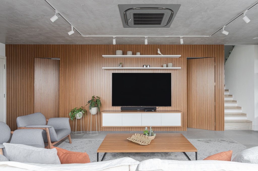 Sala de estar com parede revestida de painéis de madeira e iluminação com trilho de spots.