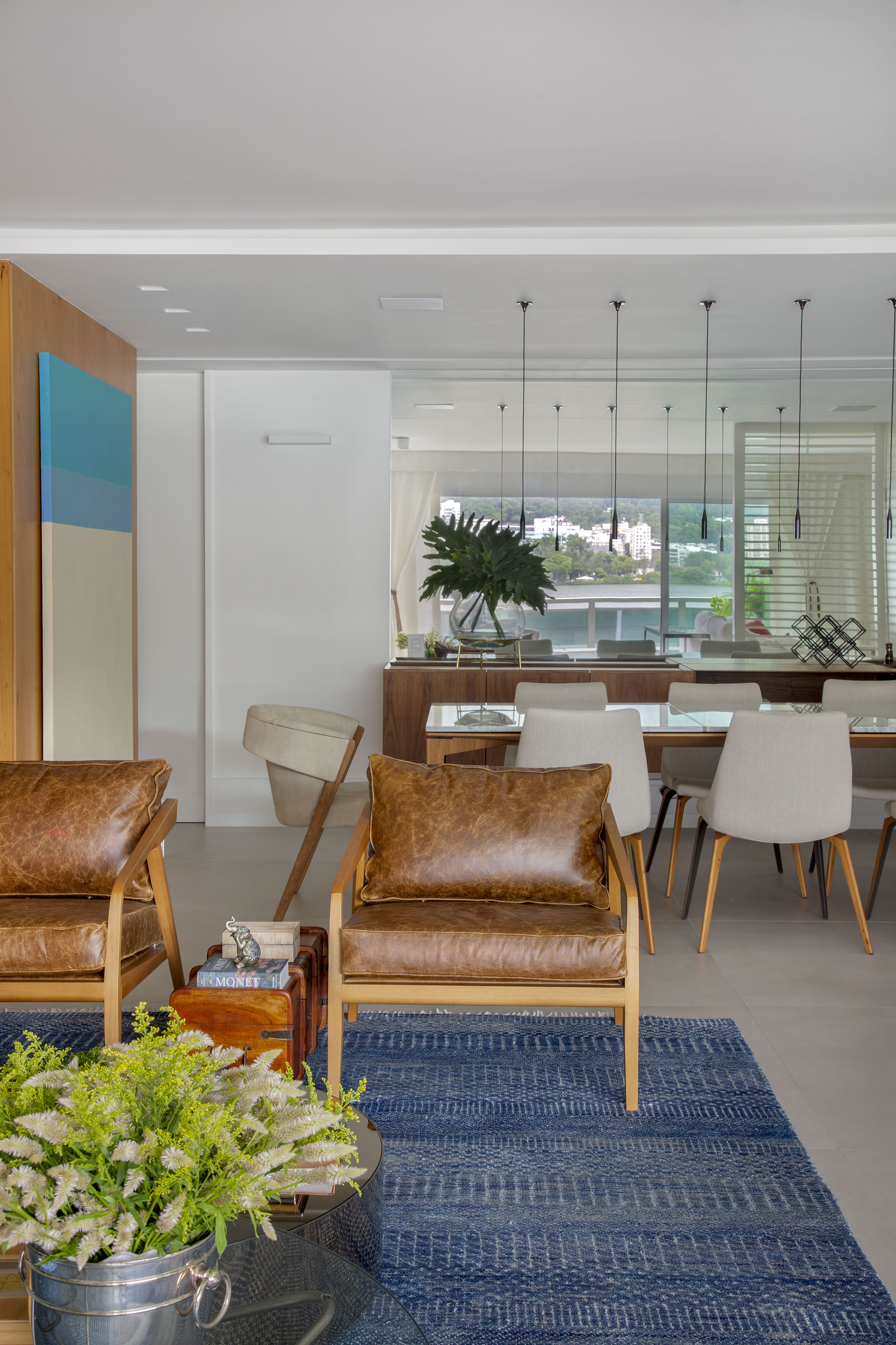 Sala de jantar integrada com sala de estar; poltrona de couro, tapete azul e mesa de jantar com cadeiras.
