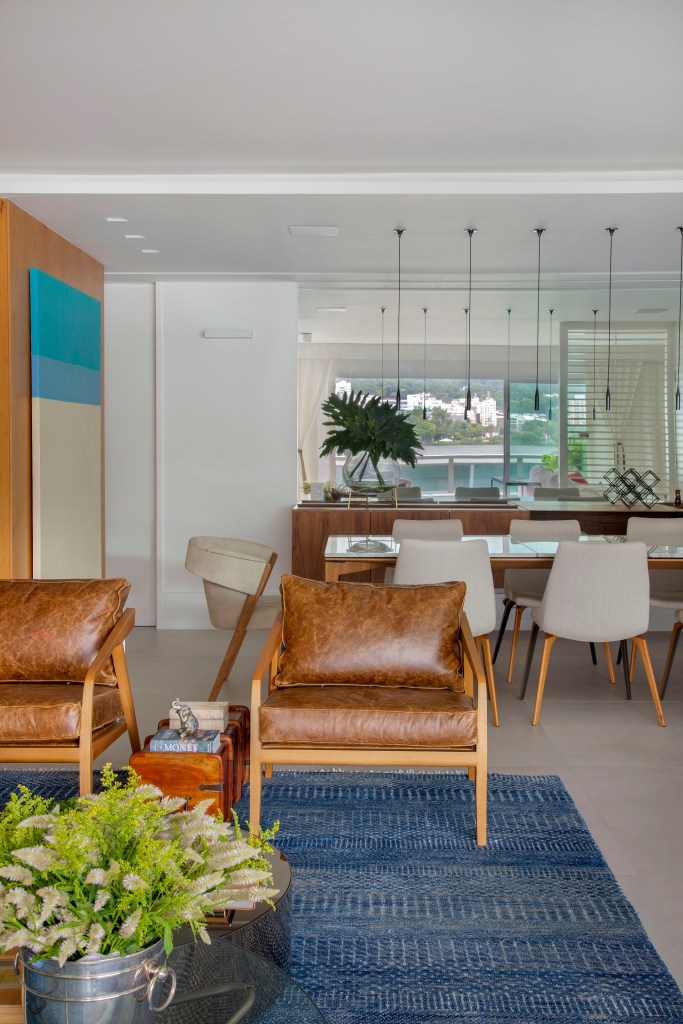 Sala de jantar integrada com sala de estar; poltrona de couro, tapete azul e mesa de jantar com cadeiras.