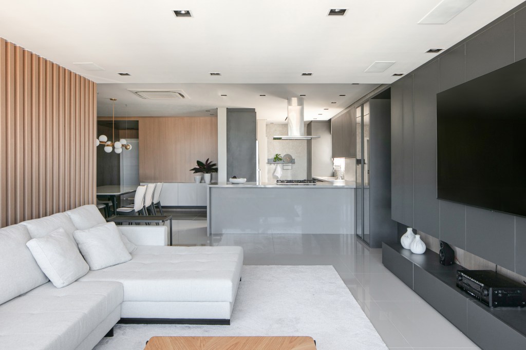 Sala de estar com piso de porcelanato cinza, sofá branco e cozinha integrada.