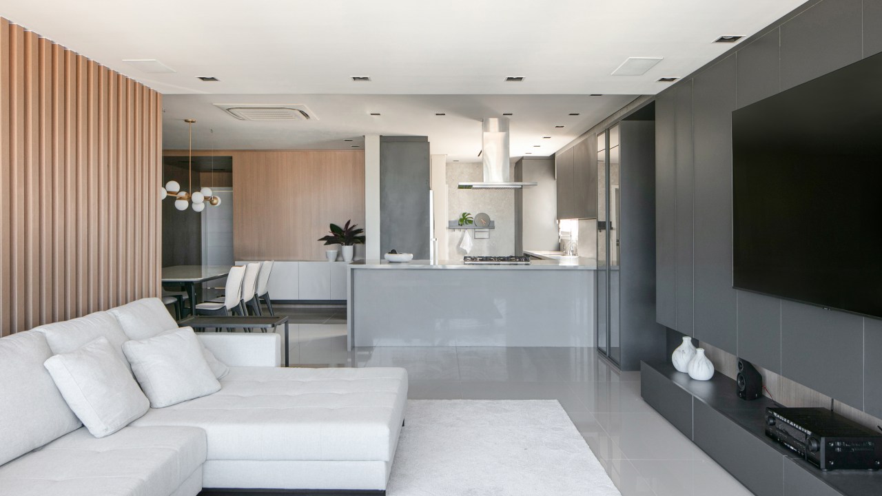 Sala de estar com piso de porcelanato cinza, sofá branco e cozinha integrada.