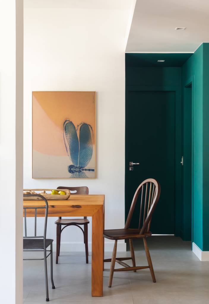 Sala de jantar com mesa de madeira e cadeiras de modelos diferentes.