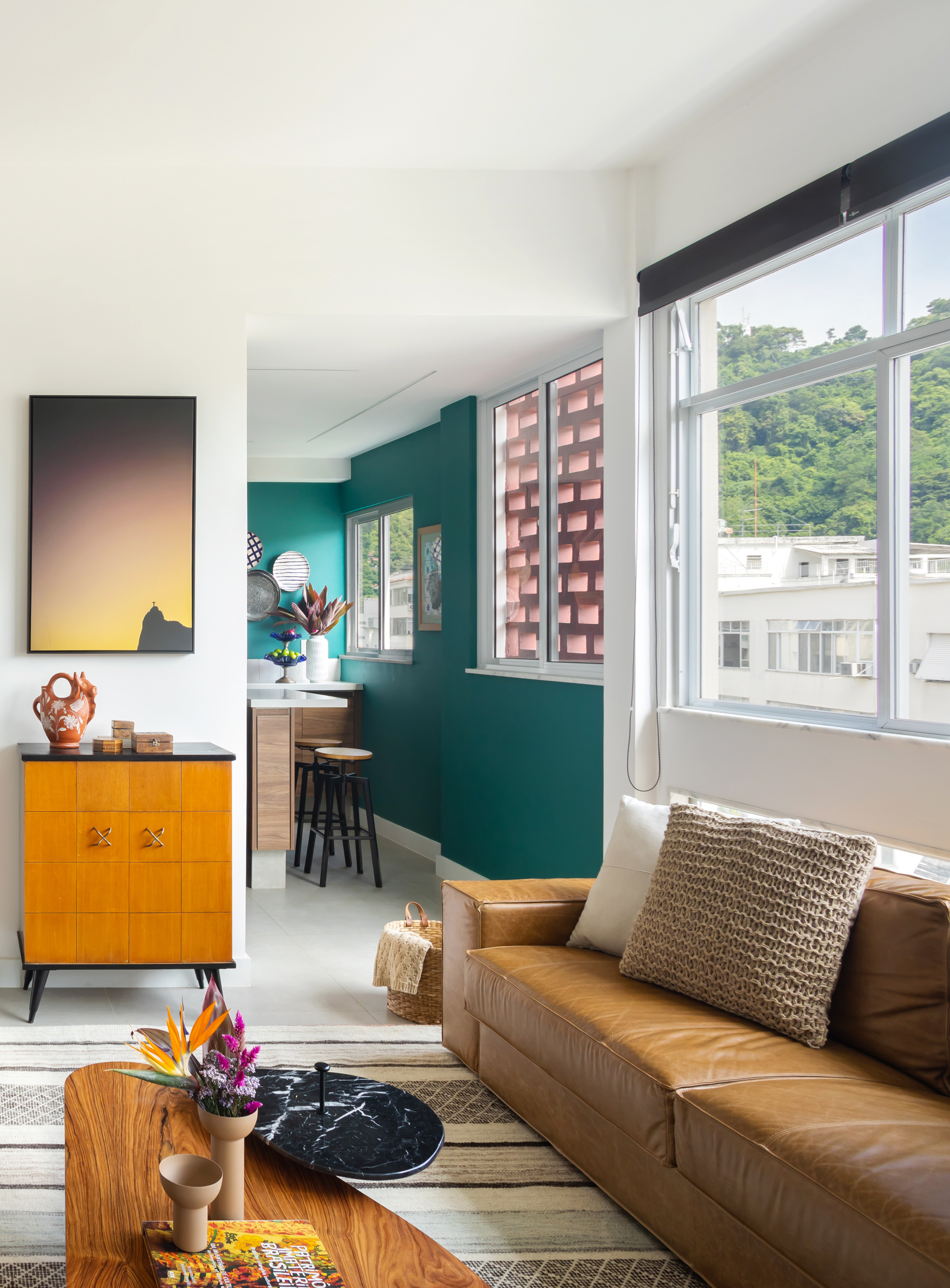 Sala de estar com sofá de couro, tapete listrado e cozinha integrada com parede verde.