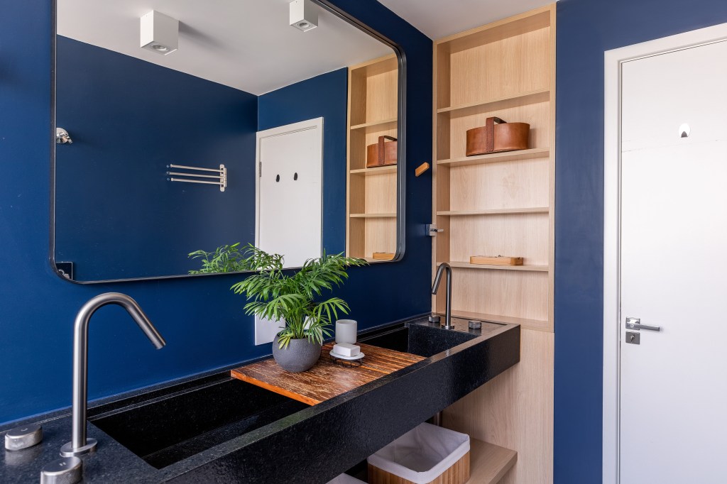 Banheiro com parede azul e bancada com cuba esculpida em quartzo.