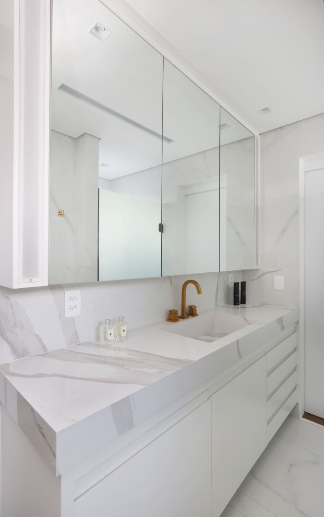 Banheiro revestido com porcelanato no padrão mármore branco e bancada com cuba esculpida.