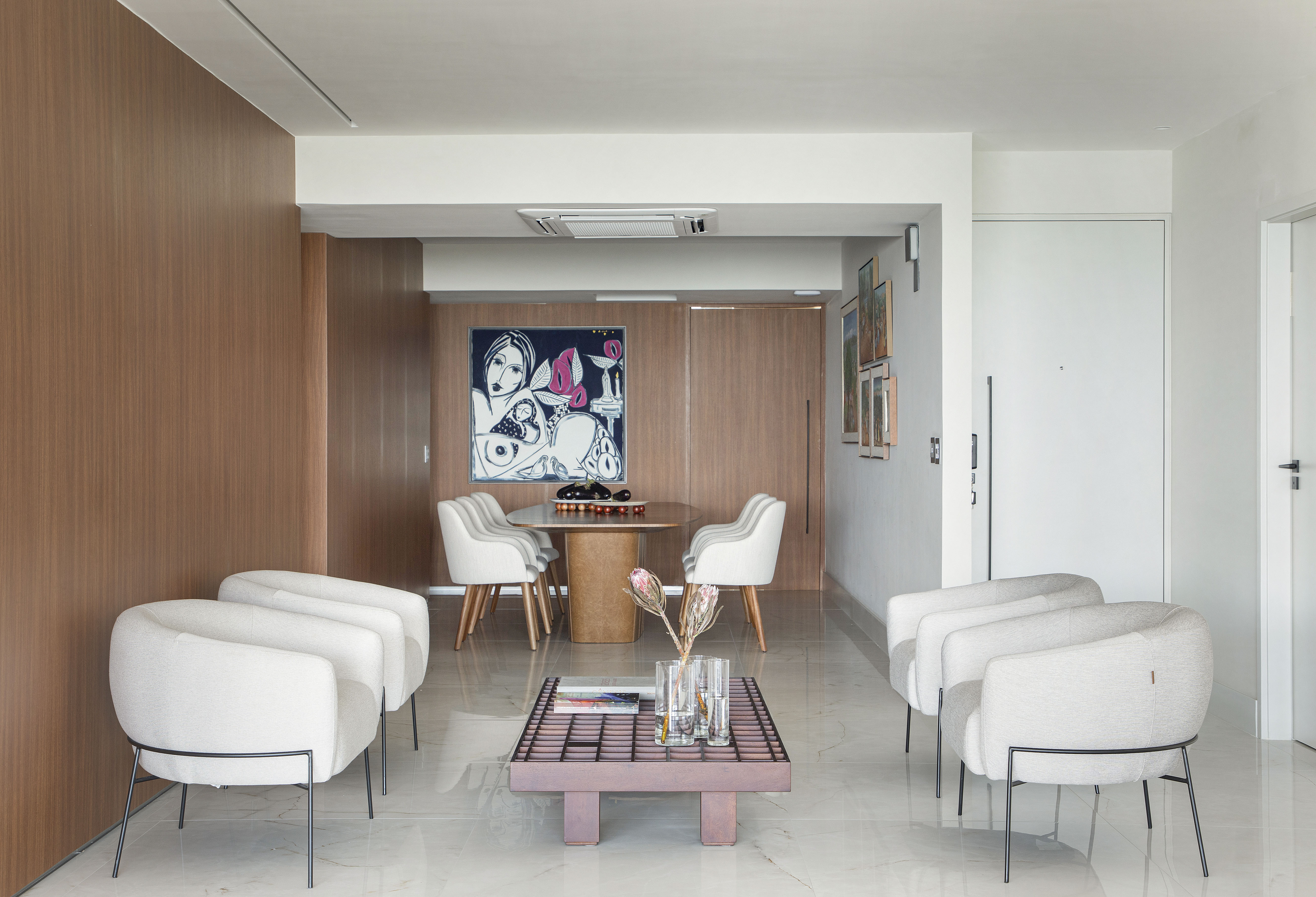 Sala de estar integrada com jantar com piso de porcelanato, poltronas brancas e mesa de centro.