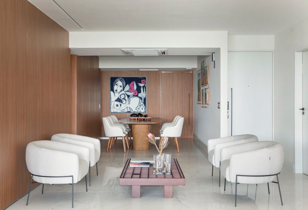 Sala de estar integrada com jantar com piso de porcelanato, poltronas brancas e mesa de centro.