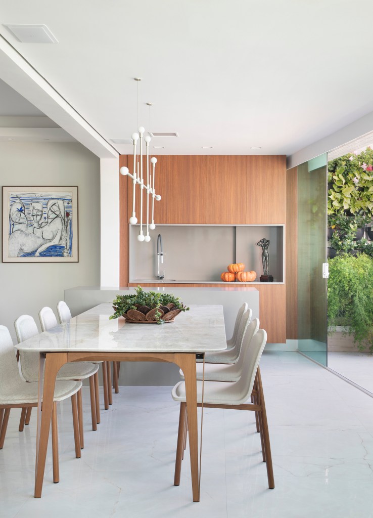 Varanda gourmet integrada com living com mesa e cadeiras brancas e jardim vertical.